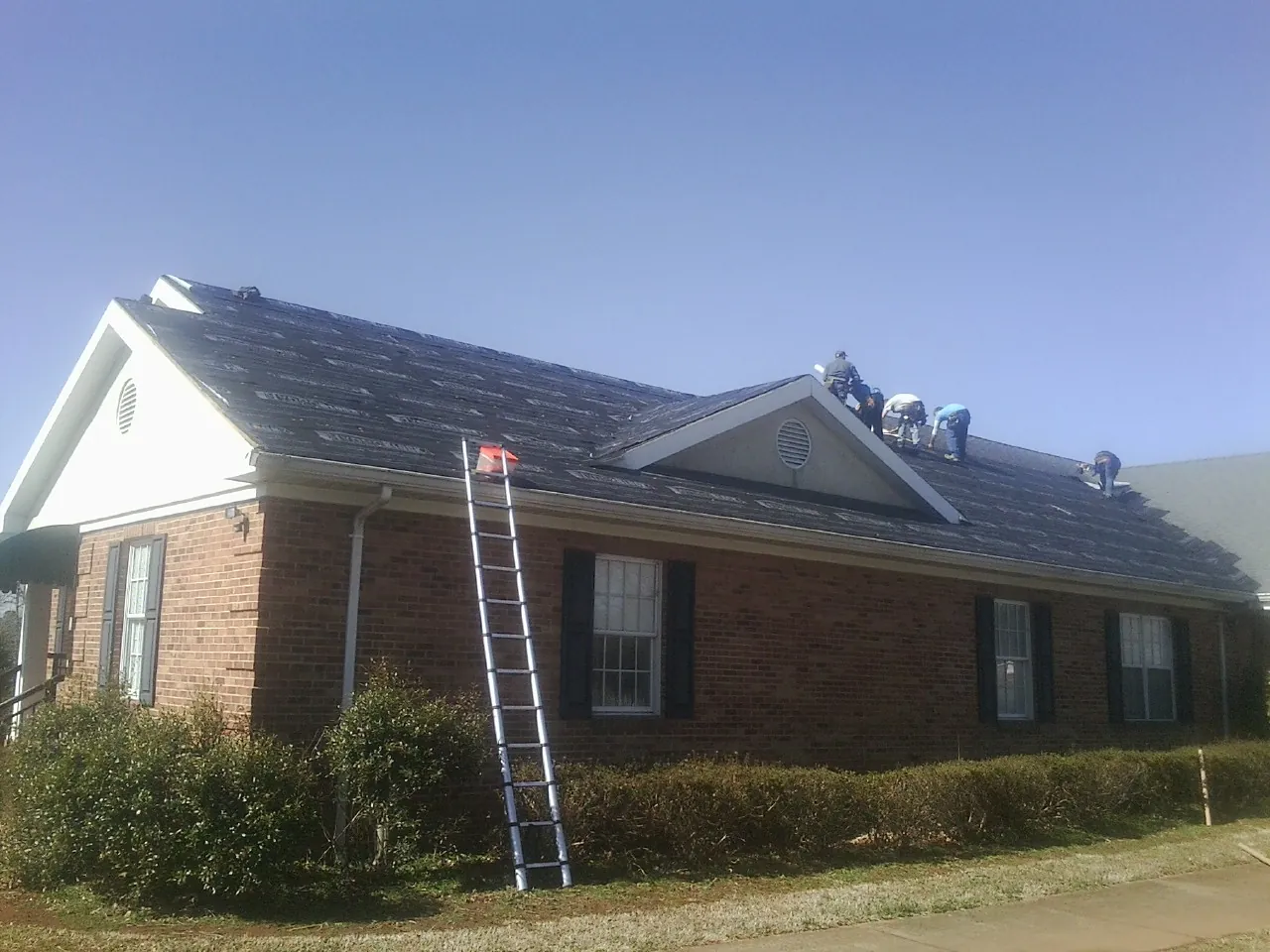 Crew tearing shingles off a brick ranch roof with a ladder set — Emergency Roof Repair work by our crew in Twin Peaks
