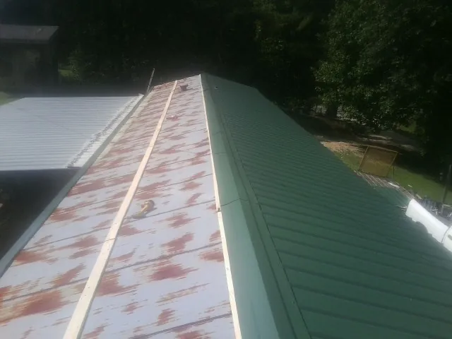 Old rusted panels beside newly installed green metal roofing — Wind Damage Roof Repair by Roofing Brothers in Twin Peaks