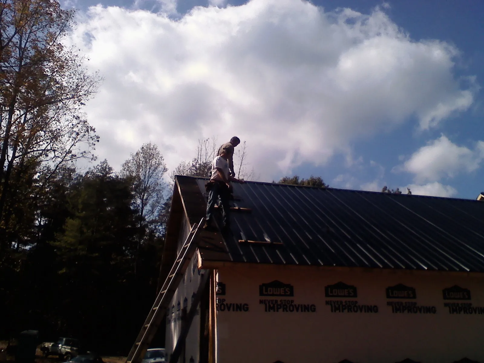 Roofer fastening dark metal panels high against a cloudy sky, from a Roof Inspection job in Twin Peaks