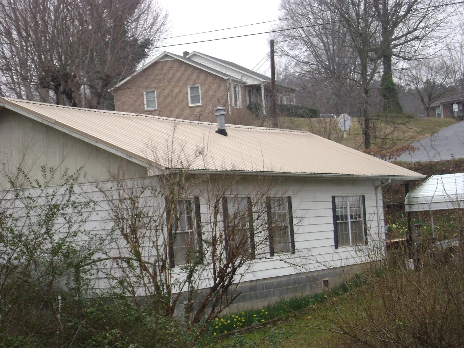 Tan metal roof on a white sided house set into a hillside — Commercial Roofing by Roofing Brothers in Twin Peaks