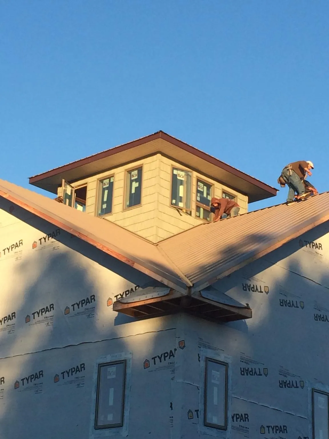 Roofers working around a rooftop cupola on a new metal roof at sunset — Roof Waterproofing in Twin Peaks by Roofing Brothers